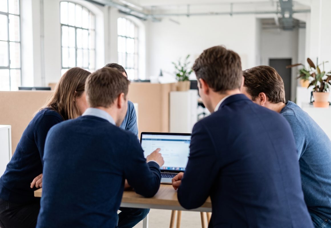 Colleagues gathered around a laptop in an open office, mid-discussion